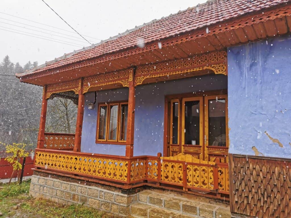 Casă tradițională restaurată cu verandă din lemn sculptat, în timpul ninsorii